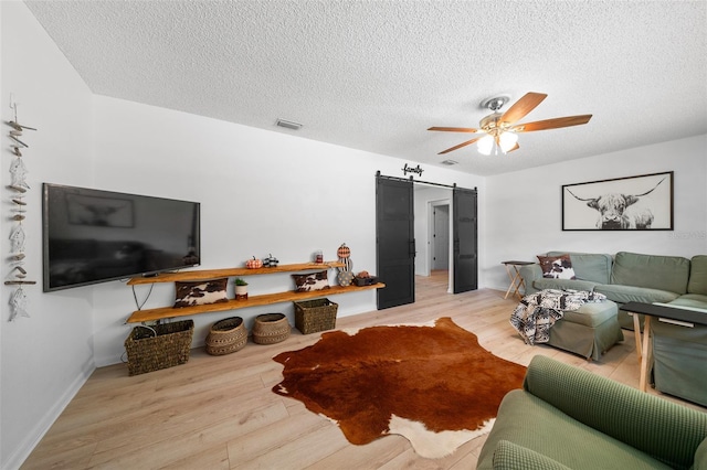 living room featuring a textured ceiling, a barn door, light hardwood / wood-style flooring, and ceiling fan