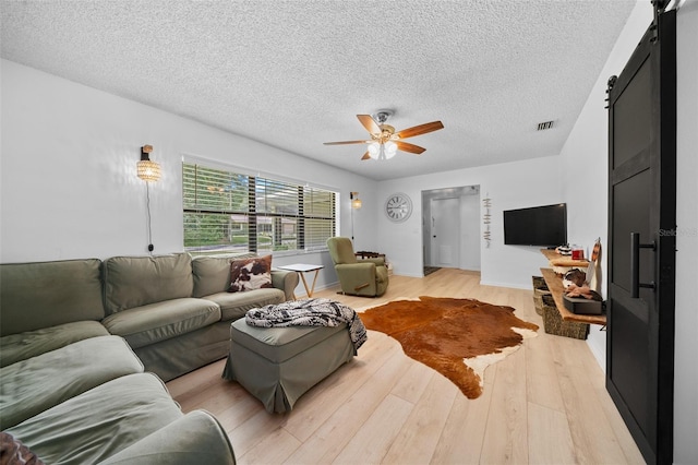 living room with a barn door, ceiling fan, light hardwood / wood-style floors, and a textured ceiling