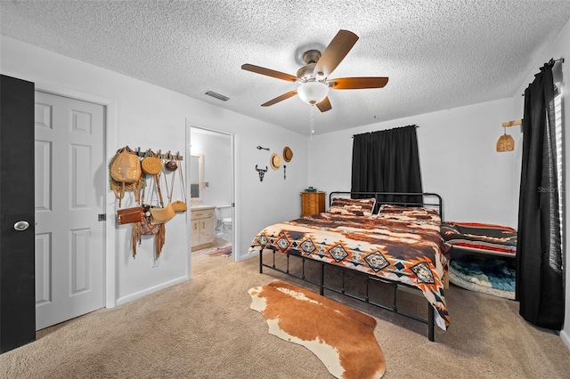 bedroom featuring ceiling fan, light colored carpet, a textured ceiling, and connected bathroom