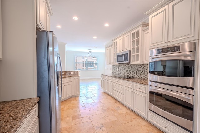 kitchen featuring light stone countertops, tasteful backsplash, stainless steel appliances, white cabinetry, and hanging light fixtures