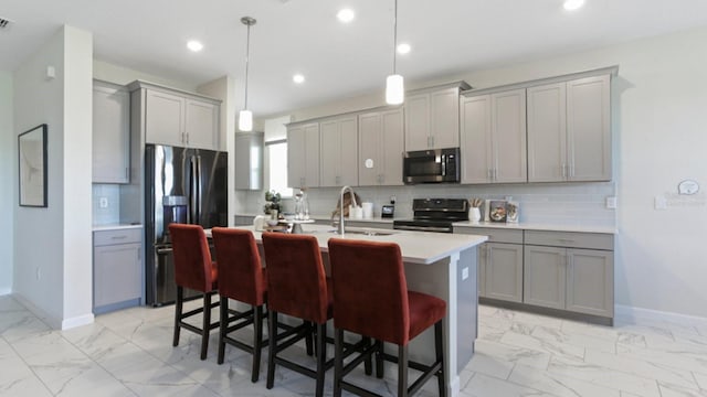 kitchen featuring gray cabinetry, sink, appliances with stainless steel finishes, decorative light fixtures, and a kitchen bar