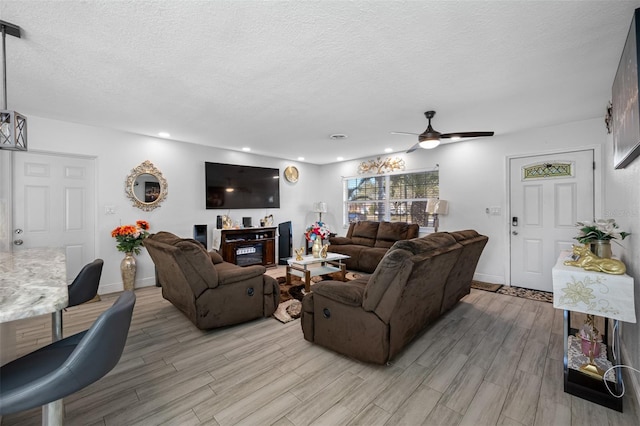 living room featuring ceiling fan, light hardwood / wood-style flooring, and a textured ceiling