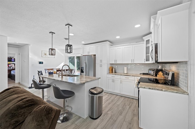 kitchen featuring sink, stainless steel appliances, an island with sink, pendant lighting, and white cabinets