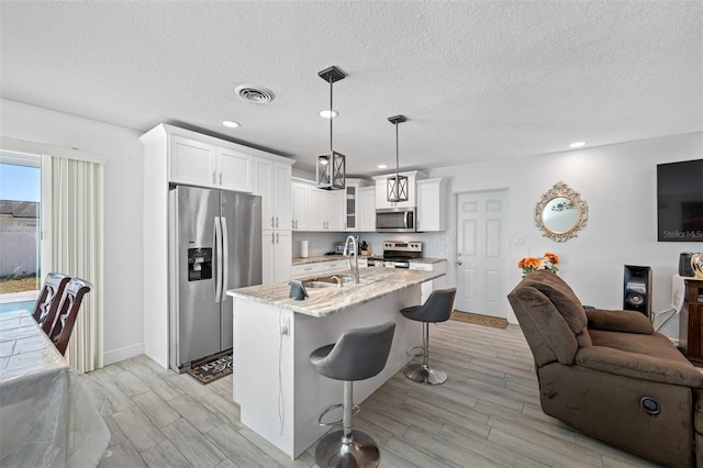 kitchen featuring sink, hanging light fixtures, light stone counters, white cabinets, and appliances with stainless steel finishes