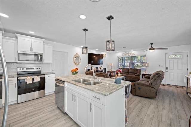 kitchen with appliances with stainless steel finishes, light wood-type flooring, ceiling fan, sink, and white cabinetry