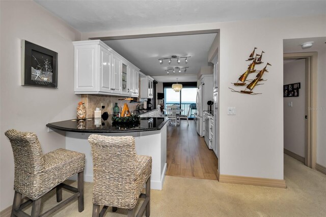 kitchen with white cabinets, tasteful backsplash, kitchen peninsula, and light hardwood / wood-style flooring