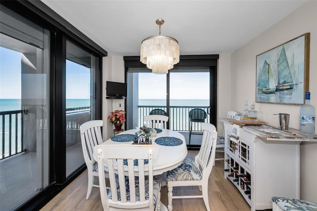 dining space featuring plenty of natural light, a water view, light wood-type flooring, and a notable chandelier