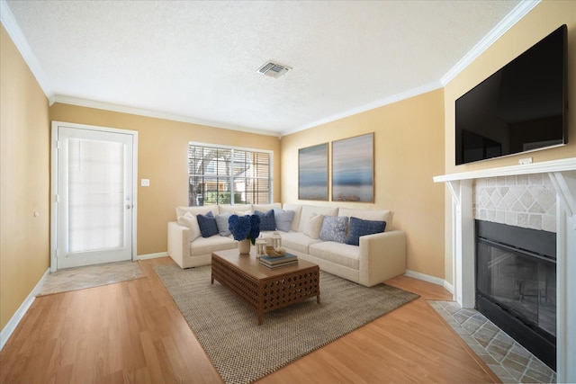 living room with a tile fireplace, crown molding, a textured ceiling, and light wood-type flooring