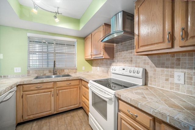 kitchen featuring white appliances, track lighting, sink, light hardwood / wood-style flooring, and wall chimney exhaust hood