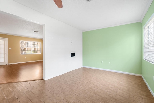 spare room featuring a textured ceiling, light wood-type flooring, plenty of natural light, and crown molding