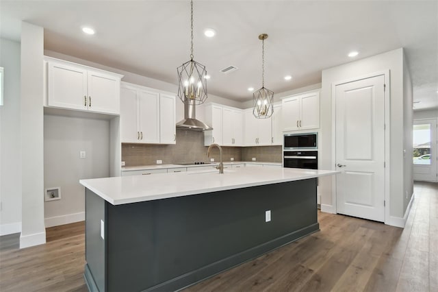 kitchen with white cabinetry, an island with sink, and wall chimney range hood