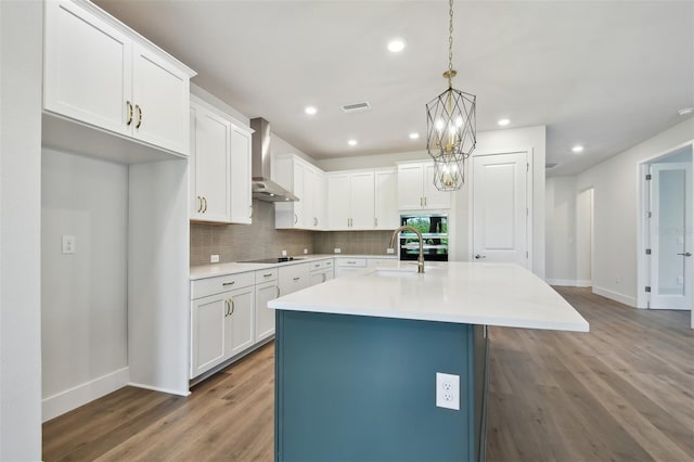 kitchen featuring tasteful backsplash, white cabinetry, wall chimney range hood, black appliances, and a center island with sink