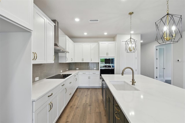 kitchen featuring pendant lighting, wall chimney range hood, sink, and white cabinets