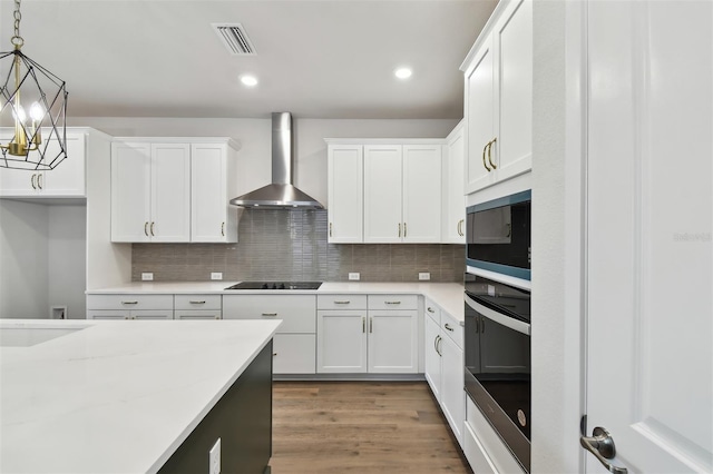 kitchen featuring built in microwave, wall chimney exhaust hood, hanging light fixtures, oven, and white cabinets