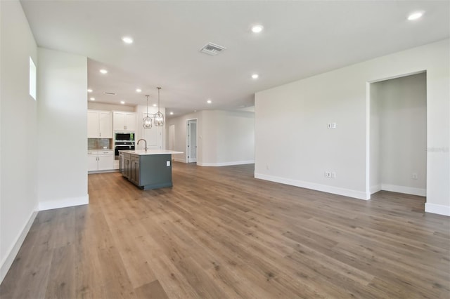 kitchen featuring pendant lighting, a kitchen island with sink, white cabinetry, stainless steel microwave, and wood-type flooring