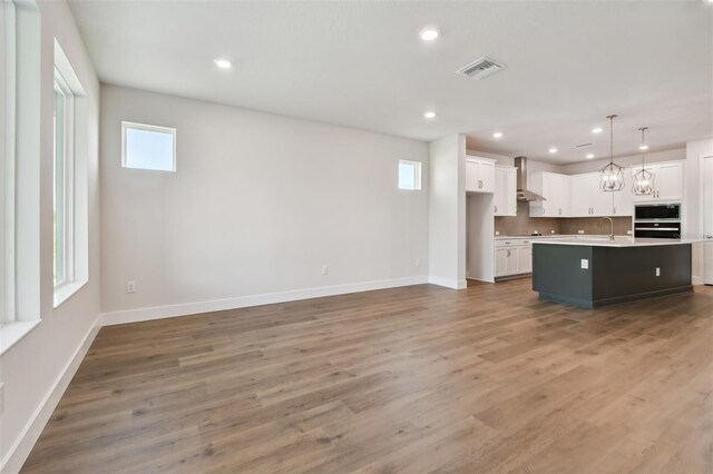 kitchen featuring pendant lighting, hardwood / wood-style flooring, a kitchen island with sink, white cabinets, and wall chimney exhaust hood