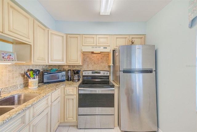 kitchen with light stone countertops, cream cabinetry, decorative backsplash, light tile patterned floors, and appliances with stainless steel finishes