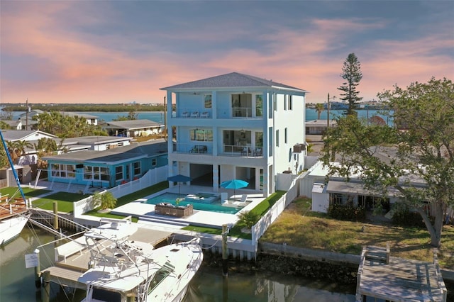 back house at dusk featuring a balcony, a water view, and a patio