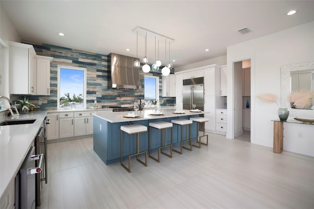 kitchen featuring appliances with stainless steel finishes, extractor fan, white cabinets, a center island, and hanging light fixtures