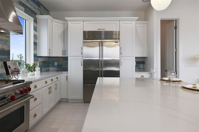 kitchen featuring decorative backsplash, premium appliances, island range hood, light tile patterned floors, and white cabinets