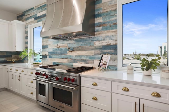 kitchen featuring white cabinets, wall chimney exhaust hood, range with two ovens, and decorative backsplash