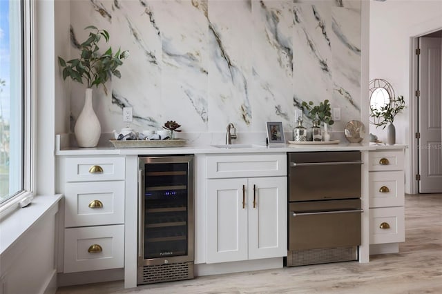 bar with white cabinets, sink, wine cooler, and light hardwood / wood-style flooring