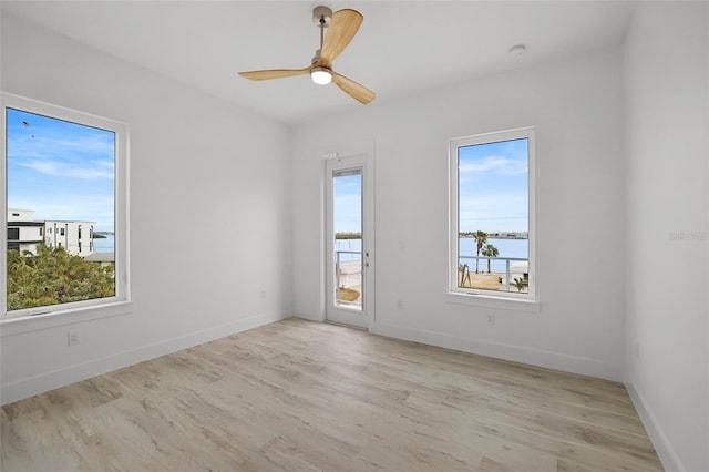 empty room with ceiling fan, a water view, and light hardwood / wood-style flooring