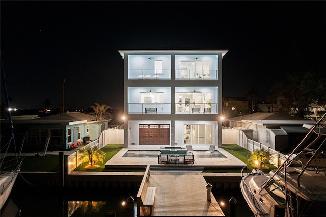 back house at night with a pool with hot tub, a patio area, and a balcony