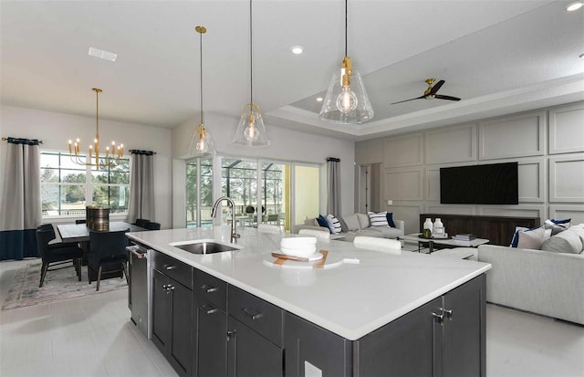 kitchen featuring decorative light fixtures, ceiling fan with notable chandelier, an island with sink, and sink