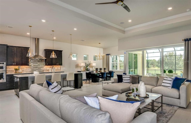 living room featuring ceiling fan with notable chandelier, ornamental molding, and sink