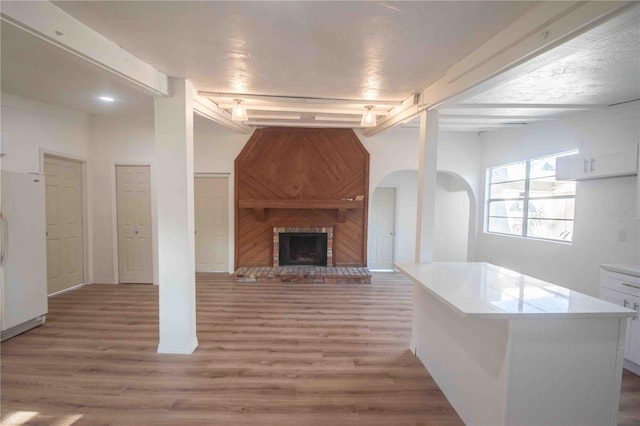 unfurnished living room featuring rail lighting, wood-type flooring, a textured ceiling, and a brick fireplace