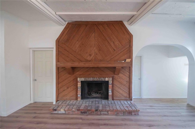 unfurnished living room with beam ceiling, hardwood / wood-style flooring, a brick fireplace, and wooden walls