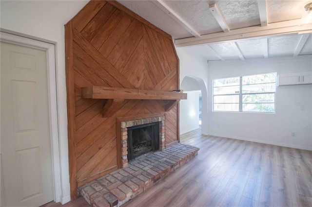 unfurnished living room featuring vaulted ceiling with beams, light wood-type flooring, a brick fireplace, and wooden walls