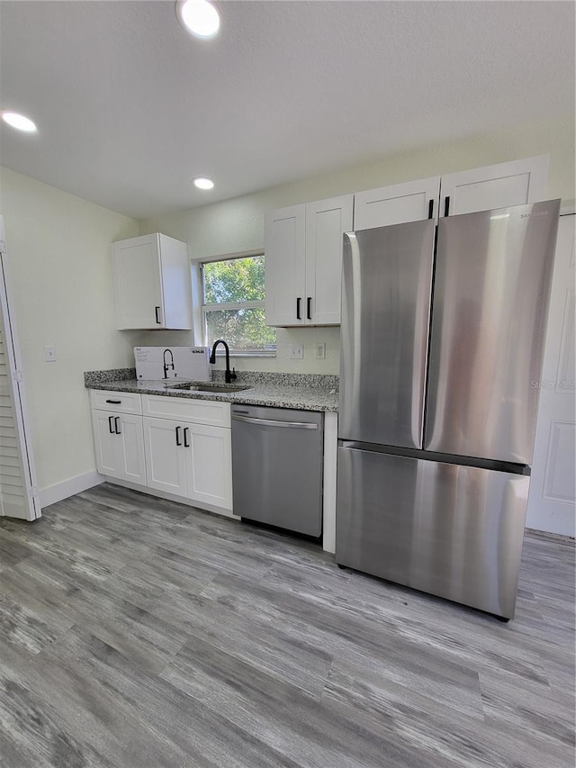 kitchen featuring white cabinets, sink, appliances with stainless steel finishes, light hardwood / wood-style floors, and light stone counters