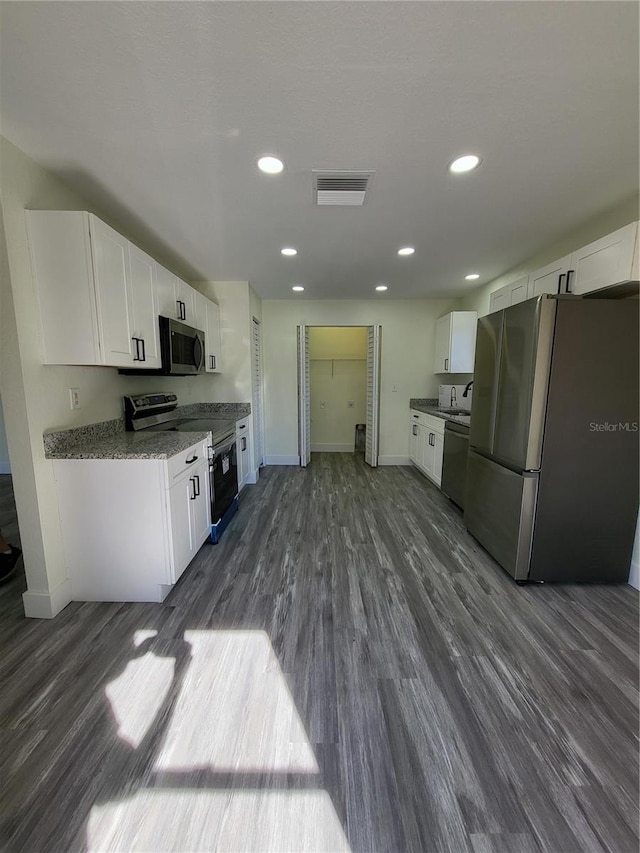 kitchen with light stone countertops, appliances with stainless steel finishes, dark wood-type flooring, sink, and white cabinets