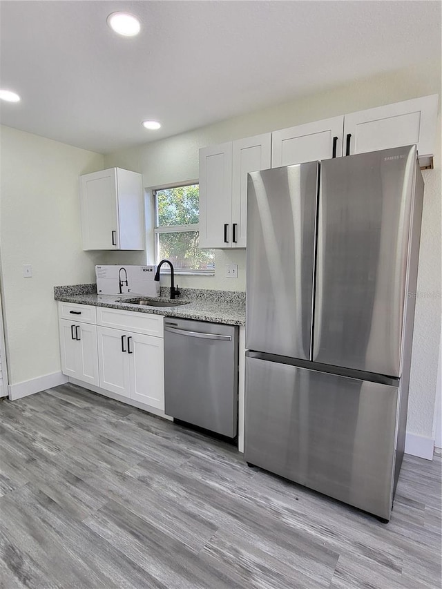 kitchen with light stone countertops, white cabinetry, sink, stainless steel appliances, and light hardwood / wood-style flooring