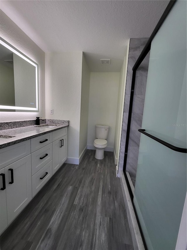 bathroom featuring vanity, a textured ceiling, a shower with door, wood-type flooring, and toilet