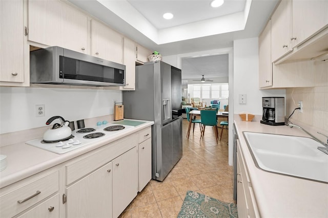 kitchen with stainless steel appliances, a raised ceiling, ceiling fan, sink, and light tile patterned floors