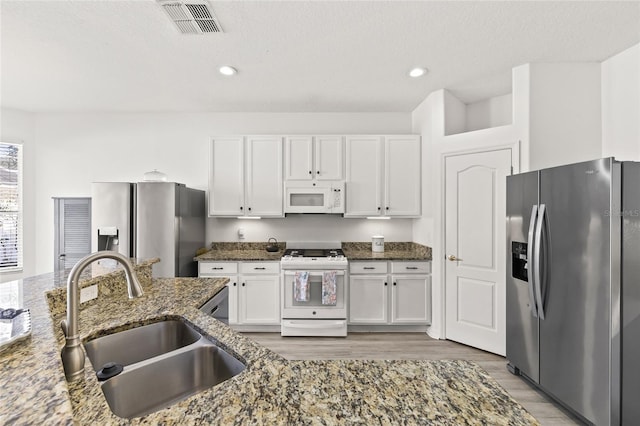 kitchen with white cabinetry, dark stone countertops, white appliances, and sink