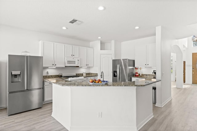 kitchen featuring a kitchen island with sink, white cabinets, dark stone counters, and stainless steel refrigerator with ice dispenser