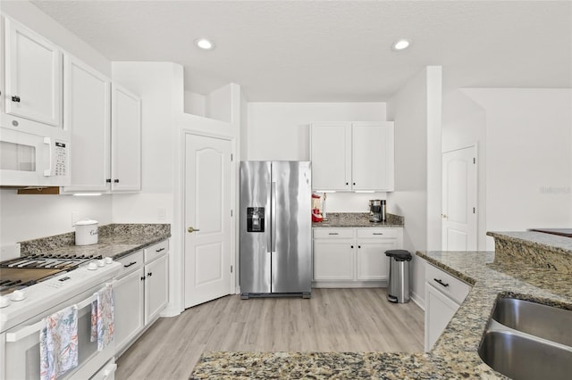 kitchen with white appliances, dark stone counters, white cabinets, sink, and light hardwood / wood-style floors