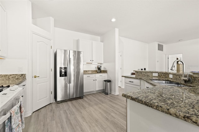 kitchen featuring light wood-type flooring, stainless steel appliances, sink, dark stone countertops, and white cabinetry