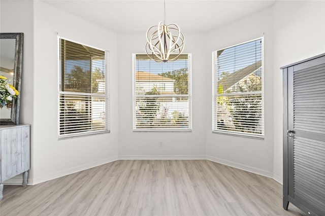 unfurnished dining area with an inviting chandelier, a healthy amount of sunlight, and light hardwood / wood-style floors