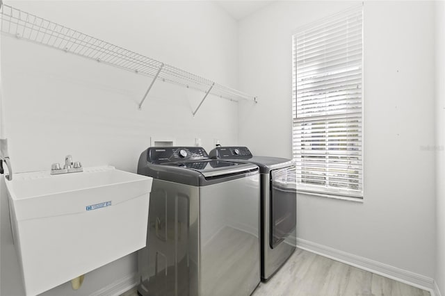 laundry room featuring washer and clothes dryer, light wood-type flooring, and sink