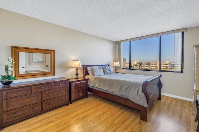 bedroom with a wall of windows, light wood-type flooring, and a textured ceiling