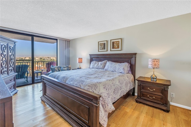 bedroom with a textured ceiling, access to exterior, a wall of windows, and light wood finished floors