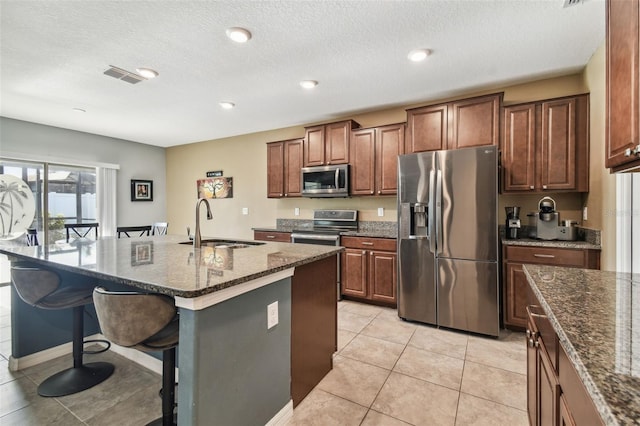 kitchen with sink, dark stone counters, a breakfast bar area, a center island with sink, and appliances with stainless steel finishes