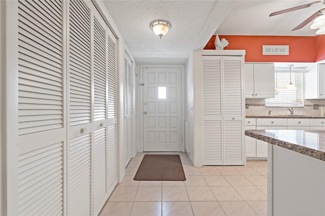 kitchen with white cabinets, hanging light fixtures, decorative backsplash, a textured ceiling, and light tile patterned flooring