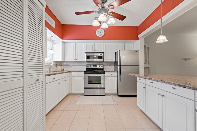 kitchen featuring decorative backsplash, appliances with stainless steel finishes, white cabinets, hanging light fixtures, and light tile patterned flooring