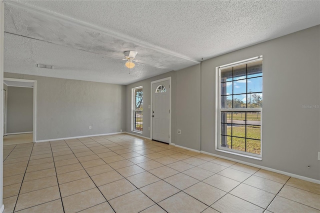 tiled spare room featuring ceiling fan, a wealth of natural light, and a textured ceiling